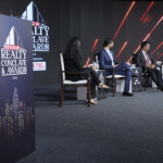Vineet Nanda speaking at an industry event with a modern Indian skyline, residential towers and smart city infrastructure in the background, representing the future of India's real estate market.