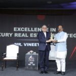 A presenter hands an award to a recipient on stage at the ET Now Realty Conclave & Awards 2026, with the backdrop highlighting excellence in luxury real estate strategy.
