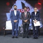 Three speakers pose on stage at the ET Now Realty Conclave & Awards 2026 event, with branded podiums, chairs and the event backdrop visible behind them.