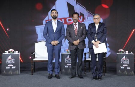 Three speakers pose on stage at the ET Now Realty Conclave & Awards 2026 event, with branded podiums, chairs and the event backdrop visible behind them.